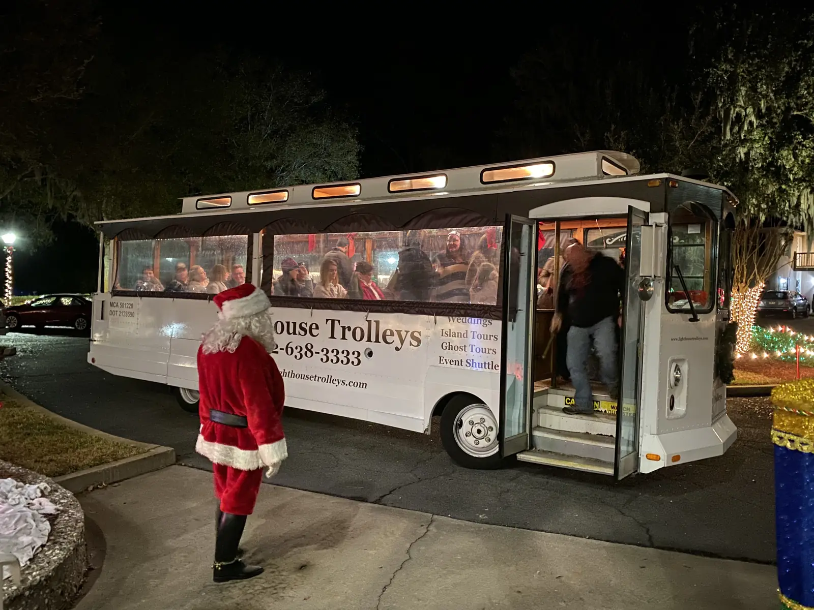 Santa greeting guests beside a trolley on the Christmas Tour of Lights