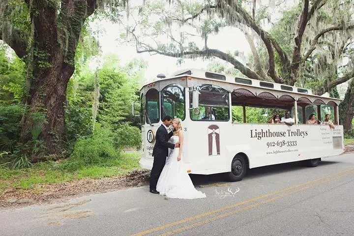 Bride and groom beside our white trolley under the live oaks